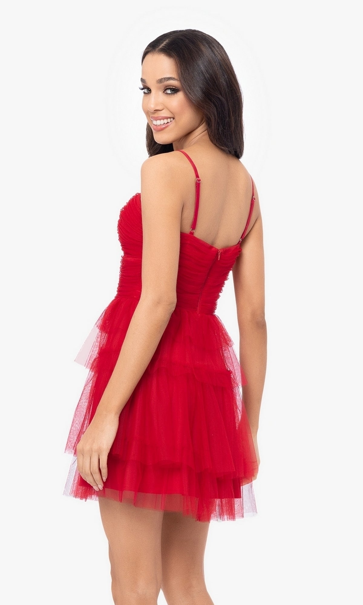 Woman wearing Cut-Out Short Ruffled Homecoming Dress 5098BN— a short red sleeveless tulle dress with spaghetti straps and ruched sweetheart bodice—smiling over her shoulder against a white background.